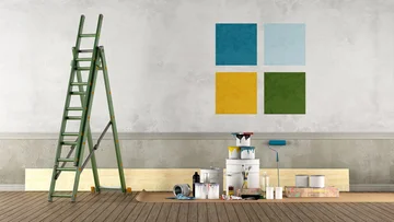 Malerwerkzeug inklusive verschiedener Farbeimer und Leiter stehen vor einer Wand auf der 4 farblich unterschiedliche Rechtecke gemalt sind.