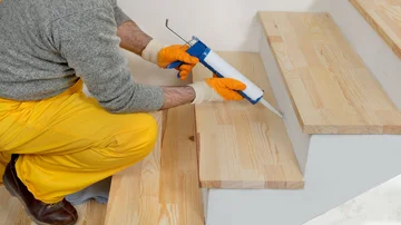 Handwerker renoviert Holztreppe, Montage neuer Holzsstufen