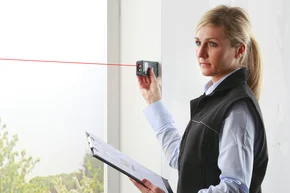 PLANUNG + AUFMASS - Decor-Union Service 124a Raumausstatterin misst mit einem professionellen Lasermessgerät das Fenster aus für Sichtschutz Sonnenschutz Gardine.